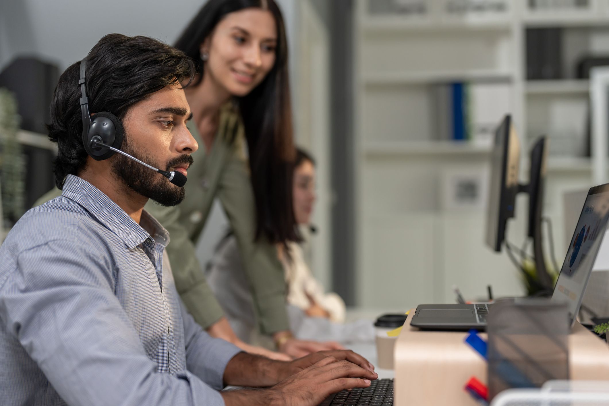 A headset-wearing agent and a colleague reviewing work together at a computer
